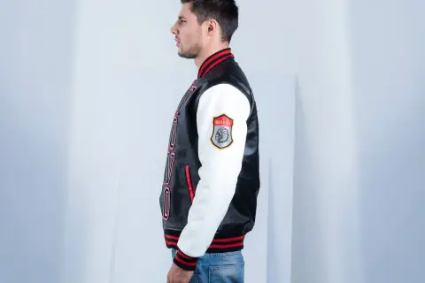 Man in profile wearing a black and white letterman jacket with red trim and a "Warrior" patch.