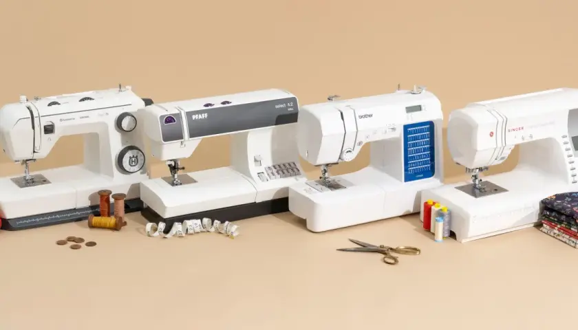 A sewing professional's dream: four white sewing machines from Husqvarna, Pfaff, Brother, and Singer, with spools of thread, fabric, and scissors.