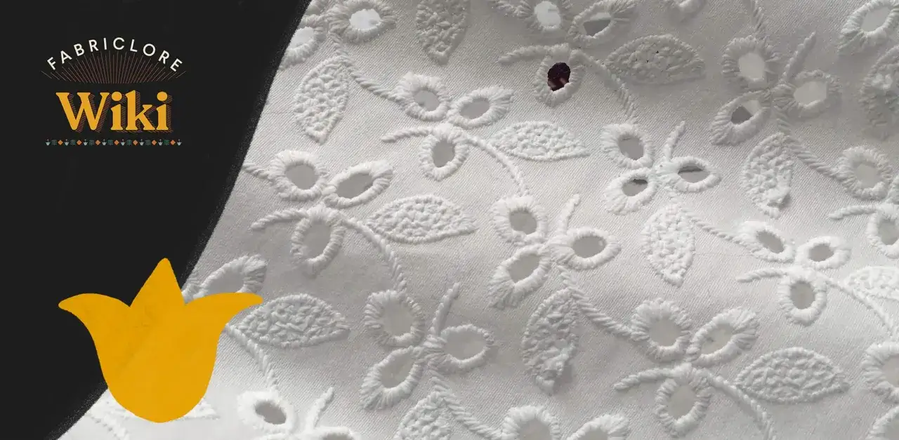 Close-up of white eyelet fabric with floral embroidery. This delicate fabric features cut-out eyelets and intricate stitching, perfect for summer dresses.