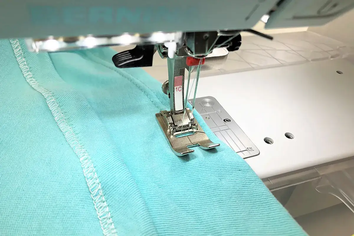 A sewing machine creates a neat double needle topstitch on a turquoise fabric.