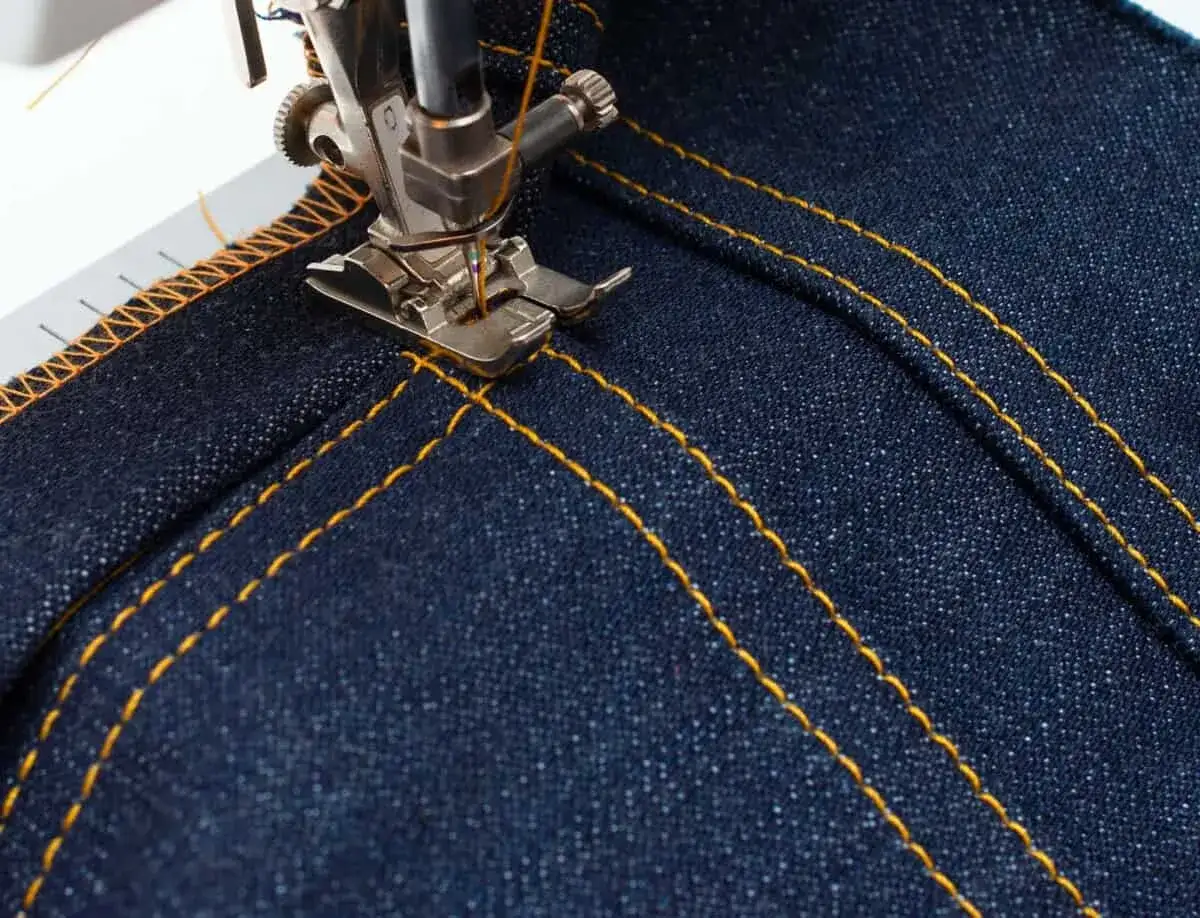 Close-up of a sewing machine stitching double yellow lines on dark denim. Perfect sewing machine settings for denim projects.