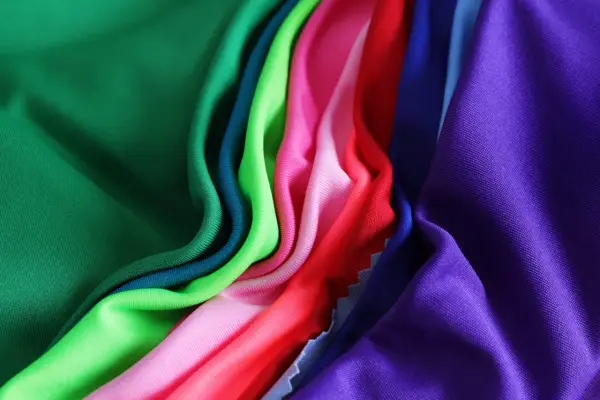 A vibrant collection of athletic wear fabric swatches in green, teal, lime, pink, red, blue, and purple, draped and folded.